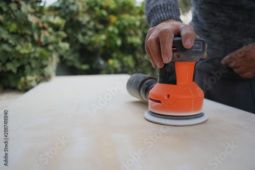 Person's hand operating an orbital sander, smoothing and preparing a wooden surface for a diy woodworking project or repair
