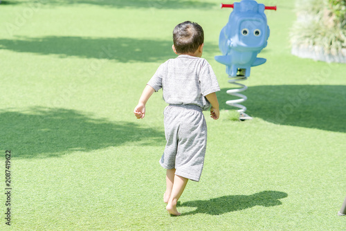Fotografie Young child running towards a blue spring rider toy in a sunny outdoor park sett