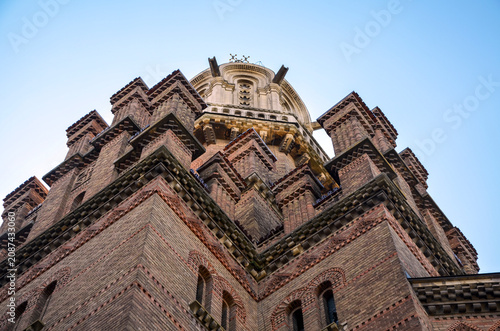 Bild auf Leinwand Low angle shot of the historic brick tower of Chernivtsi University under a blue sky with white clouds
