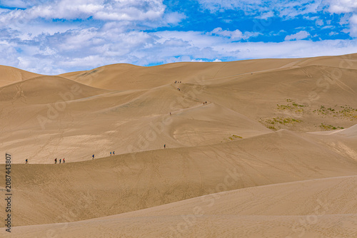 Bild auf Leinwand Groups of hikers climb the vast dune field in a line against blue sky, showing the enormous scale, Great Sand Dunes NP, Colorado