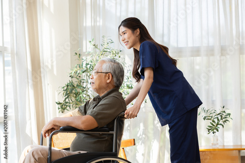 Quadro su tela Smiling young Asian female nurse pushing happy elderly senior man in wheelchair