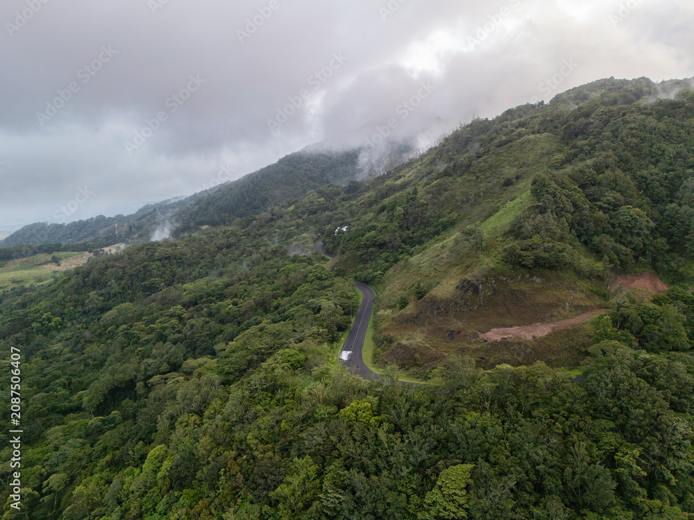 Naklejka premium Scenic view of a winding road through green hills and clouds