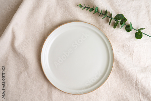 Empty Plate Mockup Concept with Ceramic Dish and Green Leaves on Linen Fabric Top View for Food Presentation and Menu Design