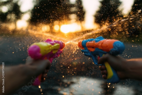 Two colorful water guns blast streams at each other during sunset