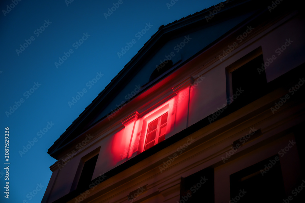 Fototapeta premium Historic manor facade dramatically illuminated with vibrant red architectural lighting against deep blue evening sky during special event
