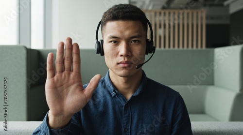 Asian support agent with headset showing stop gesture in office