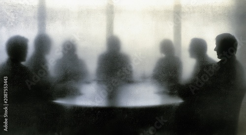 Silhouetted figures gather around a circular table, their forms blurred and indistinct
