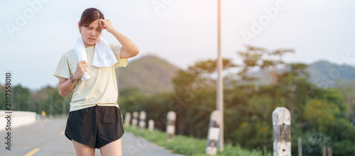 Bild auf Leinwand Exhausted Asian woman wiping sweat with a towel after jogging in the park