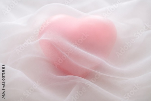 A soft pink heart shape veiled by translucent white chiffon fabric with delicate folds.