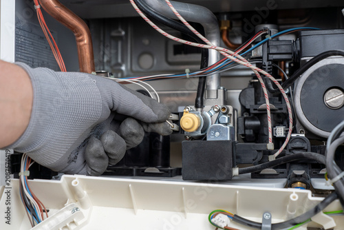фотографія Close-up of a technician hand in a protective glove connecting a wire terminal to a gas valve modulator inside an open domestic boiler during maintenance