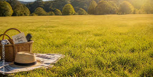 Tranquil Father's Day Picnic Scene with Hat and Basket on Sunlit Meadow for Celebratory Outdoor Gatherings