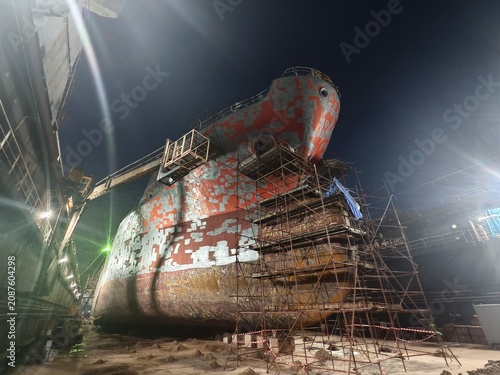 Large cargo ship under intensive maintenance in a dry dock at night.