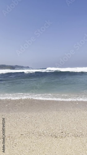 Vertical shot of ocean waves breaking on a tropical sandy beach