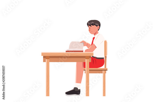 Schoolboy sitting at wooden desk reading textbook classroom learning