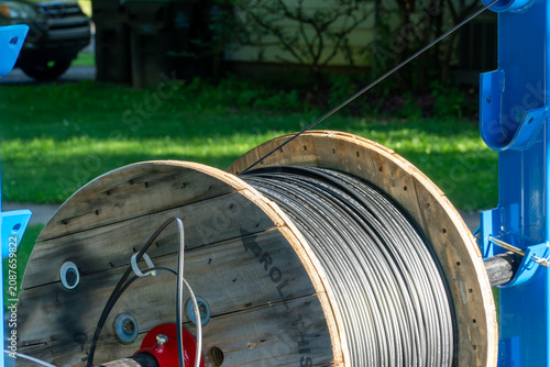 Принти на полотні Large wooden spool unwinding new black fiber optic cable for high-speed internet and telecommunications infrastructure upgrade, supported by blue industrial equipment outdoors on a sunny day