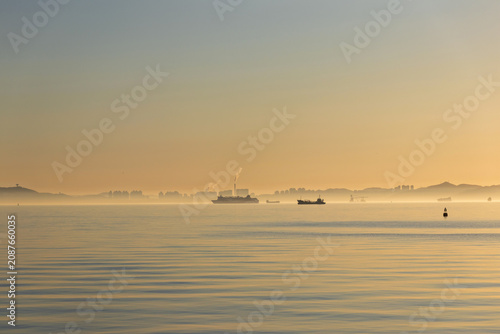Calm sea horizon cargo ship silhouette at sunrise misty coastal landscape peaceful in the Venice Water City area, Dalian City, Liaoning Province, China