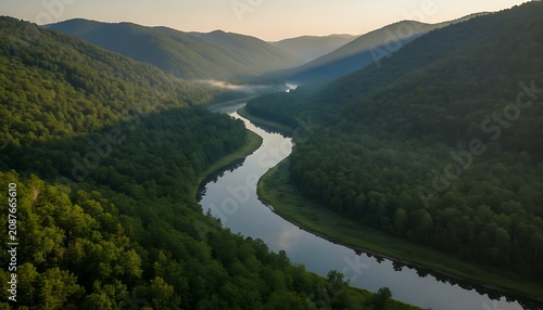 Aerial view of a winding river flowing through a deep valley surrounded by dense green forest mountains under a soft morning sky with light mist settling in the lowlands and wallpaper background