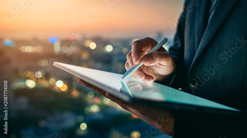Professional Businessman Using Digital Tablet and Stylus Pen for Remote Work Against Cityscape Skyline at Sunset
