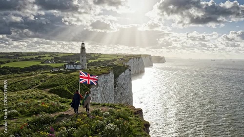 Couple standing on white cliffs of dover with uk flag and lighthouse at sunset, scenic british coastal landscape and travel destination