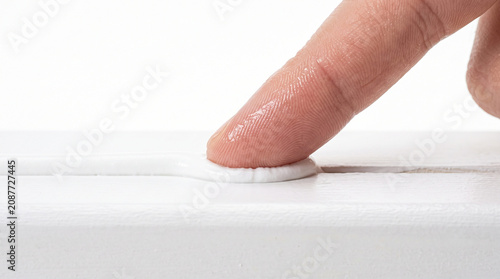 Finger smoothing white caulk sealant on wooden joint edge