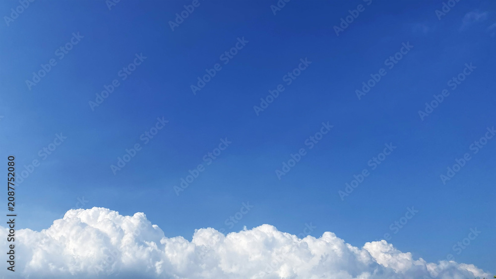 Fotografie Deep blue summer sky background with lower fluffy clouds