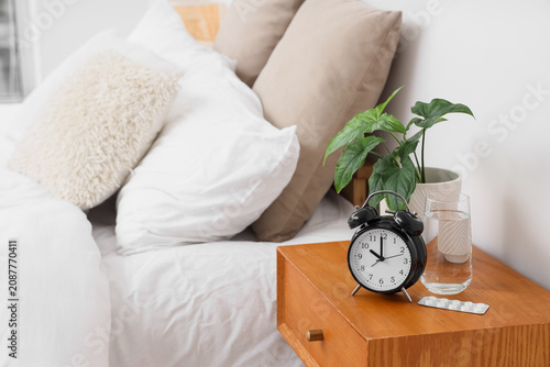 Konstfotografi Alarm clock with pills, glass of water and plant on table in bedroom