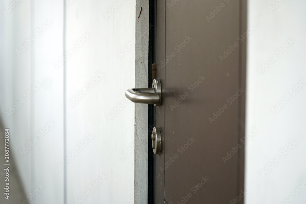 Fototapeta premium Modern stainless steel door handle with keyhole on a dark brown wooden door close up view, minimalist interior design elements for residential house or office apartment building architecture.
