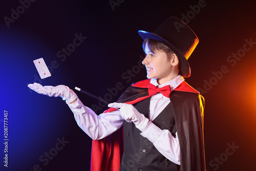 Фотография Little magician with wand and levitating playing card on dark background