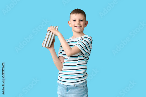 Cute little boy holding books against color background