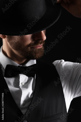 Handsome young man in formal clothes with hat against black background