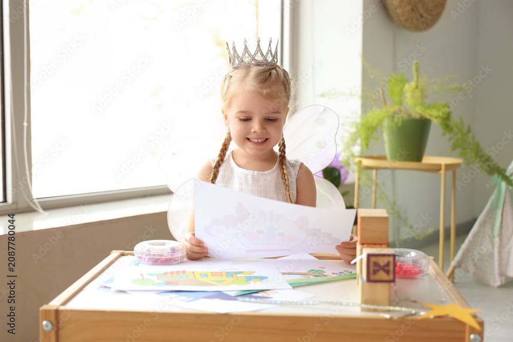 Obraz premium Cute little girl dressed as fairy with drawing at home