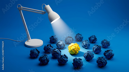 Desk lamp shining light on a unique yellow crumpled paper ball among blue ones, concept for great idea, creativity, and standing out from the crowd.