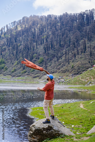 Man throwing orange jacket by Kareri Lake in Dharamshala Himachal Pradesh with mountain scenery
