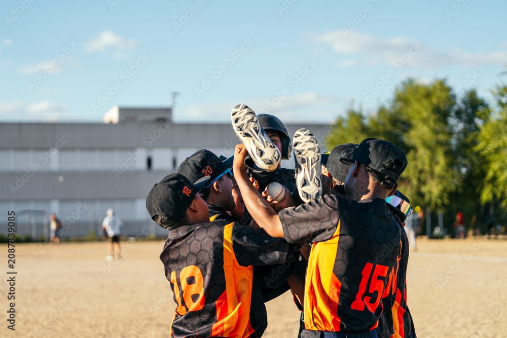 Fototapeta premium Young baseball players huddling together and lifting a teammate in the air, celebrating a win on the field