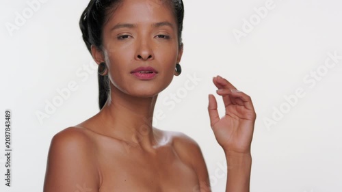 Medium close-up of south american woman light brown complexion touches her chin evoking soft skin on light grey background | Skin care advertisement