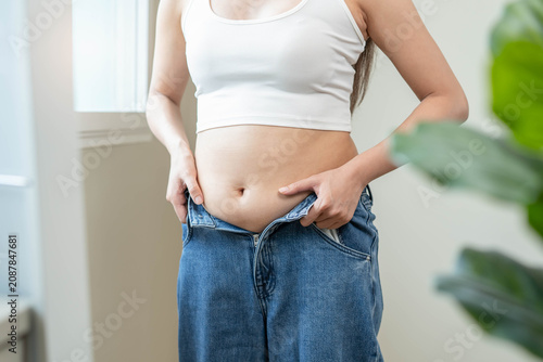 Foto Overweight female trying to button up tight denim trousers after weight gain