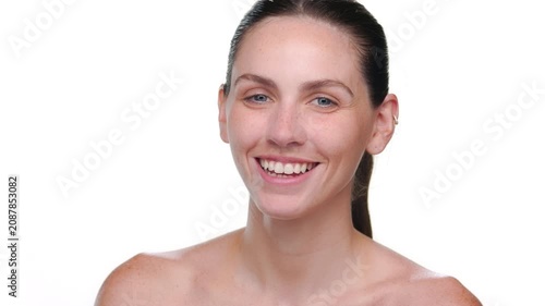 Closeup shot of fair-skinned freckled Spanish woman with blue eyes and brown hair smiles widely for the camera on light background | Face care commercial