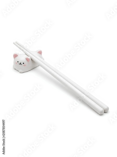 White ceramic chopsticks rest on a cat-shaped holder. The chopsticks are sleek and minimalist, complementing the charming design of the cat rest, which features a smiling face with pink ears and cheek