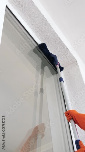 Professional window cleaning service. Worker uses long pole to clean high windows. Bright indoor environment with natural light. Vertical cleaning technique enhances efficiency.