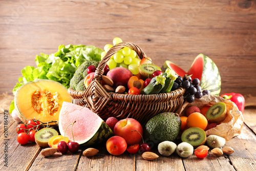 Abundant assortment of fresh fruits and vegetables in wicker basket on wood