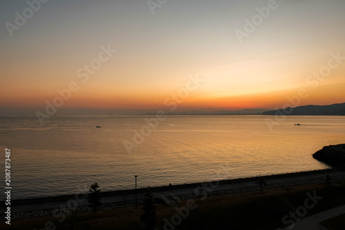 Wide angle view of a beautiful orange sunrise over the sea, mountains, and a curved coastline.