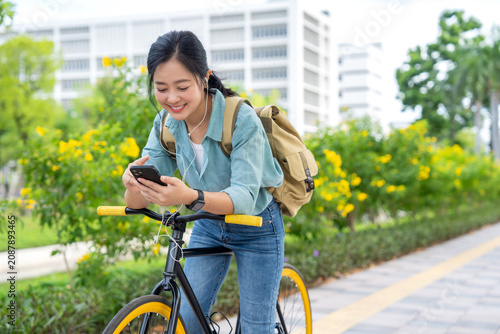 Asian woman stands near a bicycle in a city park and is using her cell phone.