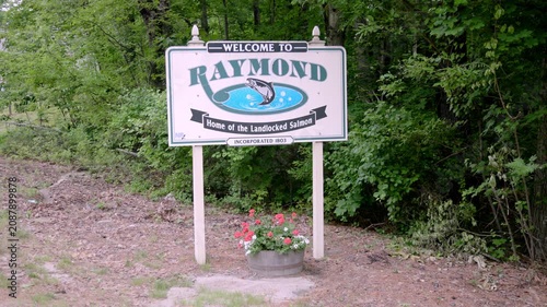 Raymond Maine welcome sign featuring landlocked salmon emblem along a rural New England roadside