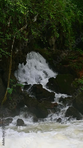 Scenic view of a natural forest waterfall cascading down rocky terrain surrounded by vibrant green foliage and tropical vegetation.