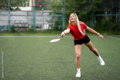 Young woman playing badminton on outdoor court. Active girl hitting shuttlecock with racket.