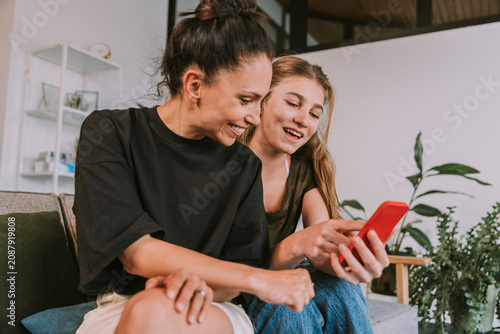 Smiling female friends looking at smart phone while sitting at home