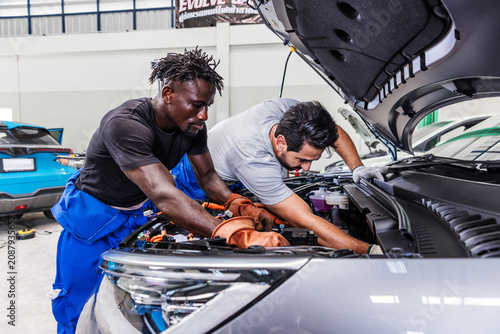 Photos Professional EV technicians collaborating to diagnose and resolve an electrical problem in a modern electric vehicle service workshop