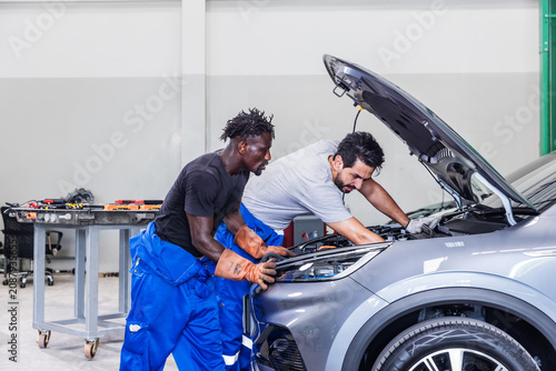 Photography Professional EV technicians collaborating to diagnose and resolve an electrical problem in a modern electric vehicle service workshop