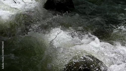 Close-up of powerful mountain river stream rushing over dark rocks with white water foam and splashes. Fast-flowing fresh water in a natural river creating bubbles and splashes in the forest.