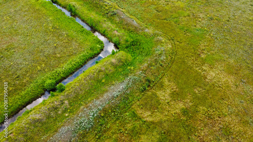 Canvastavla Aerial top-down view of a narrow drainage ditch or small stream winding through a lush green field